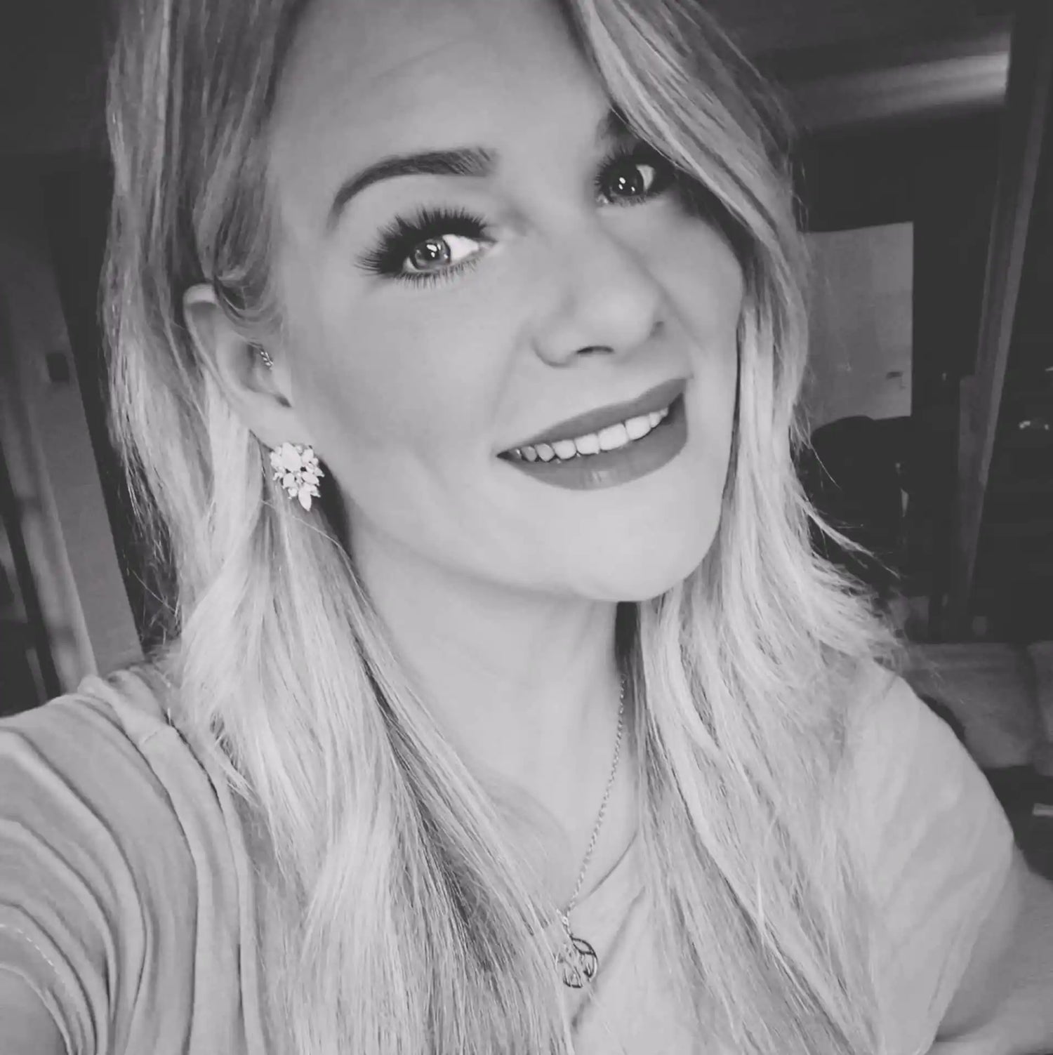 Een lachende vrouw met lang blond haar, draag een sierlijke oorbellen en een ketting.